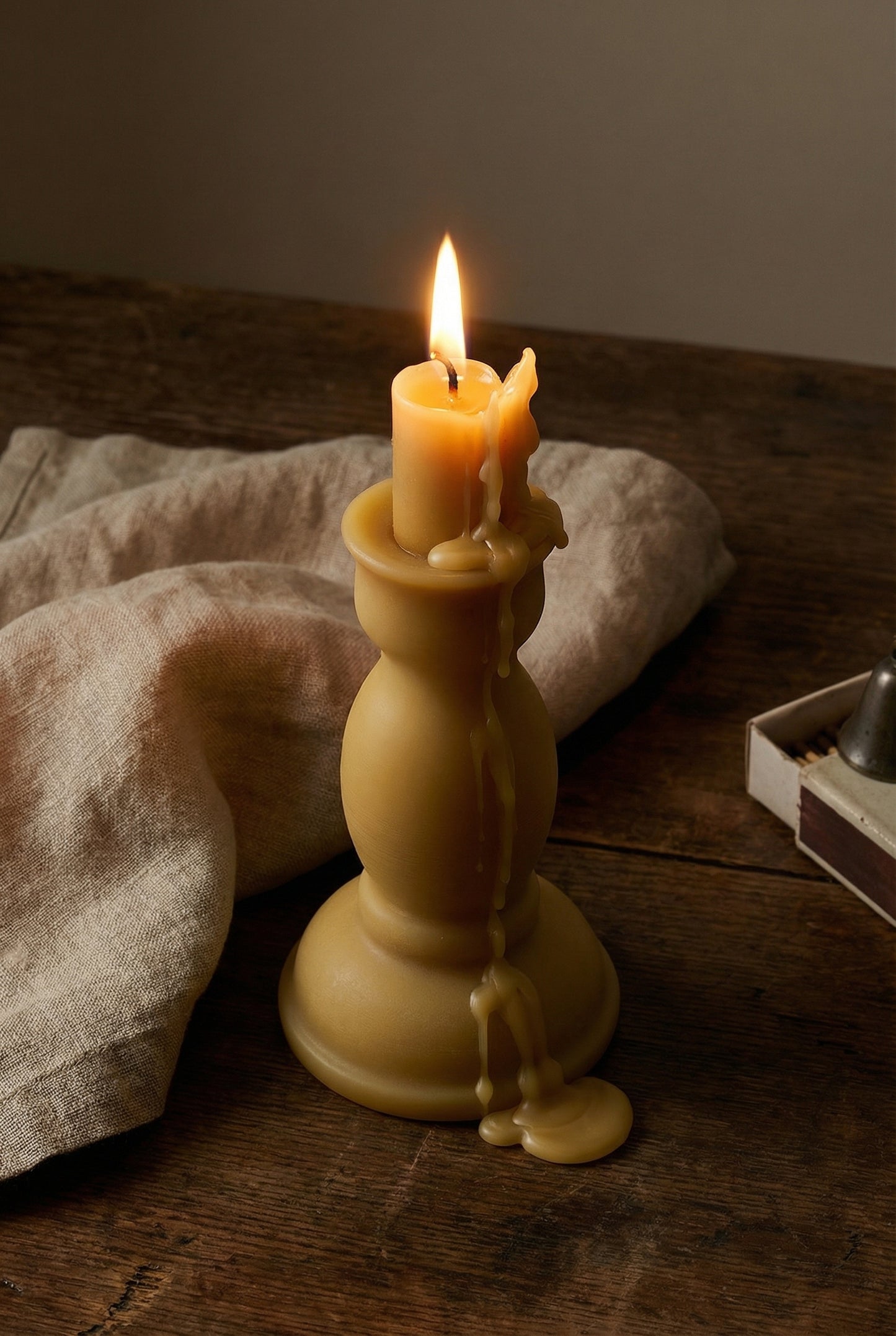 Pillar beeswax candle melting, linen, matches, wooden table