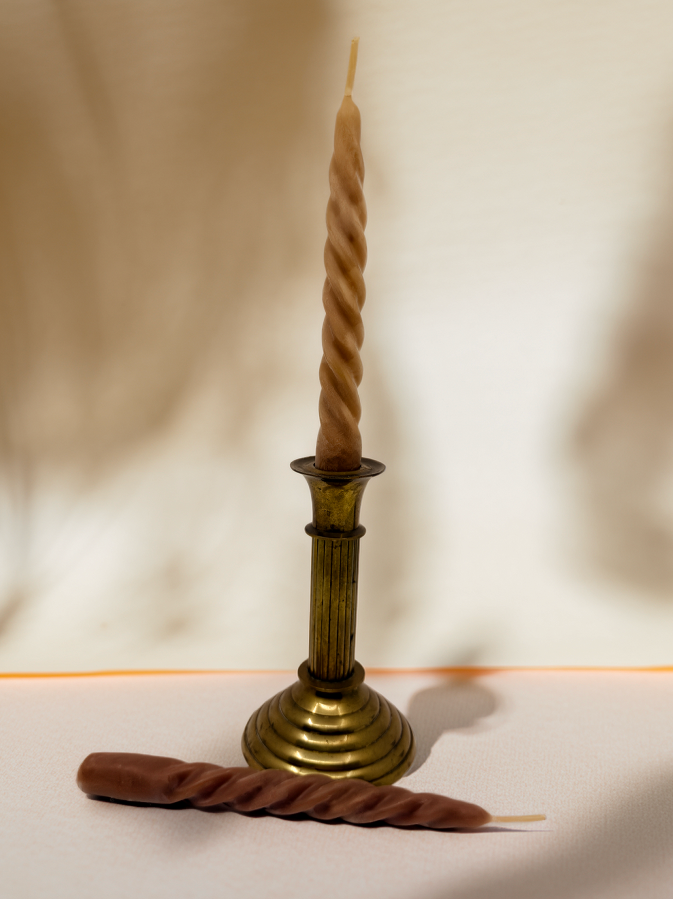 Brass candlestick holder with a twisted candle on a plain background