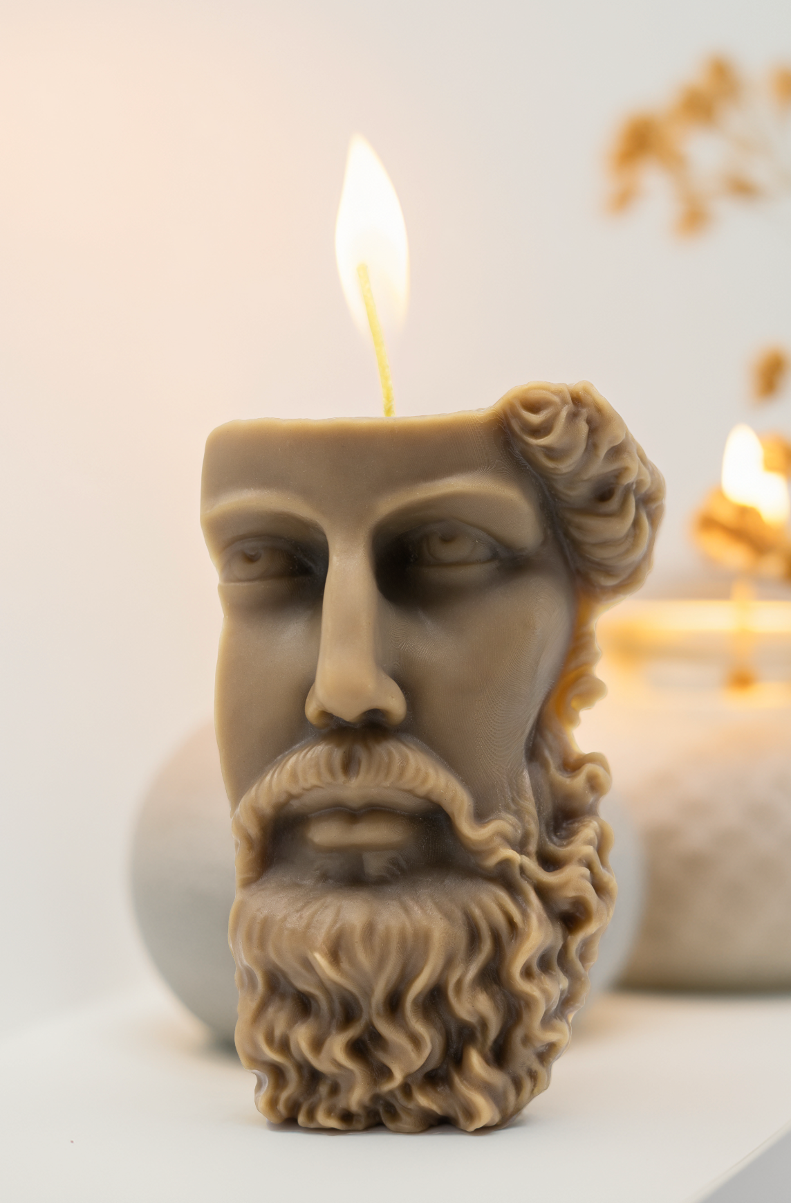 Candle shaped like a face with a beard, lit on a neutral background