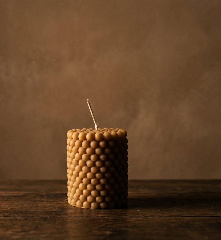 Beeswax candle with a textured surface on a wooden table against a dark background
