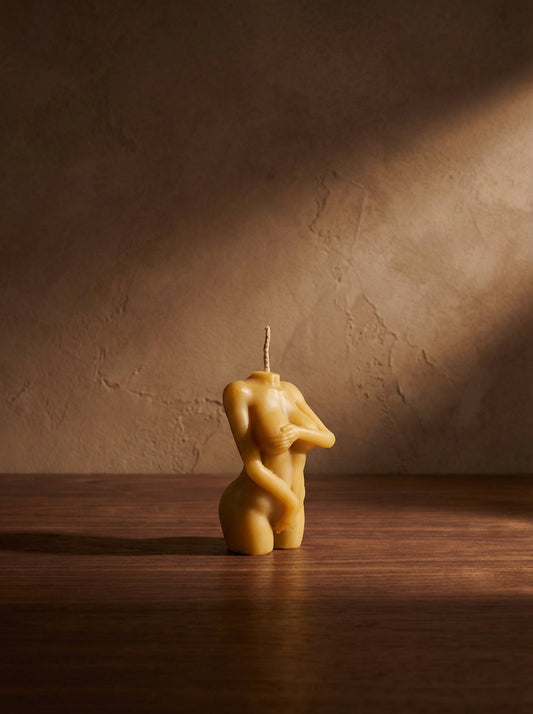 Beige candle shaped like a nude figure on a wooden surface with a brown background
