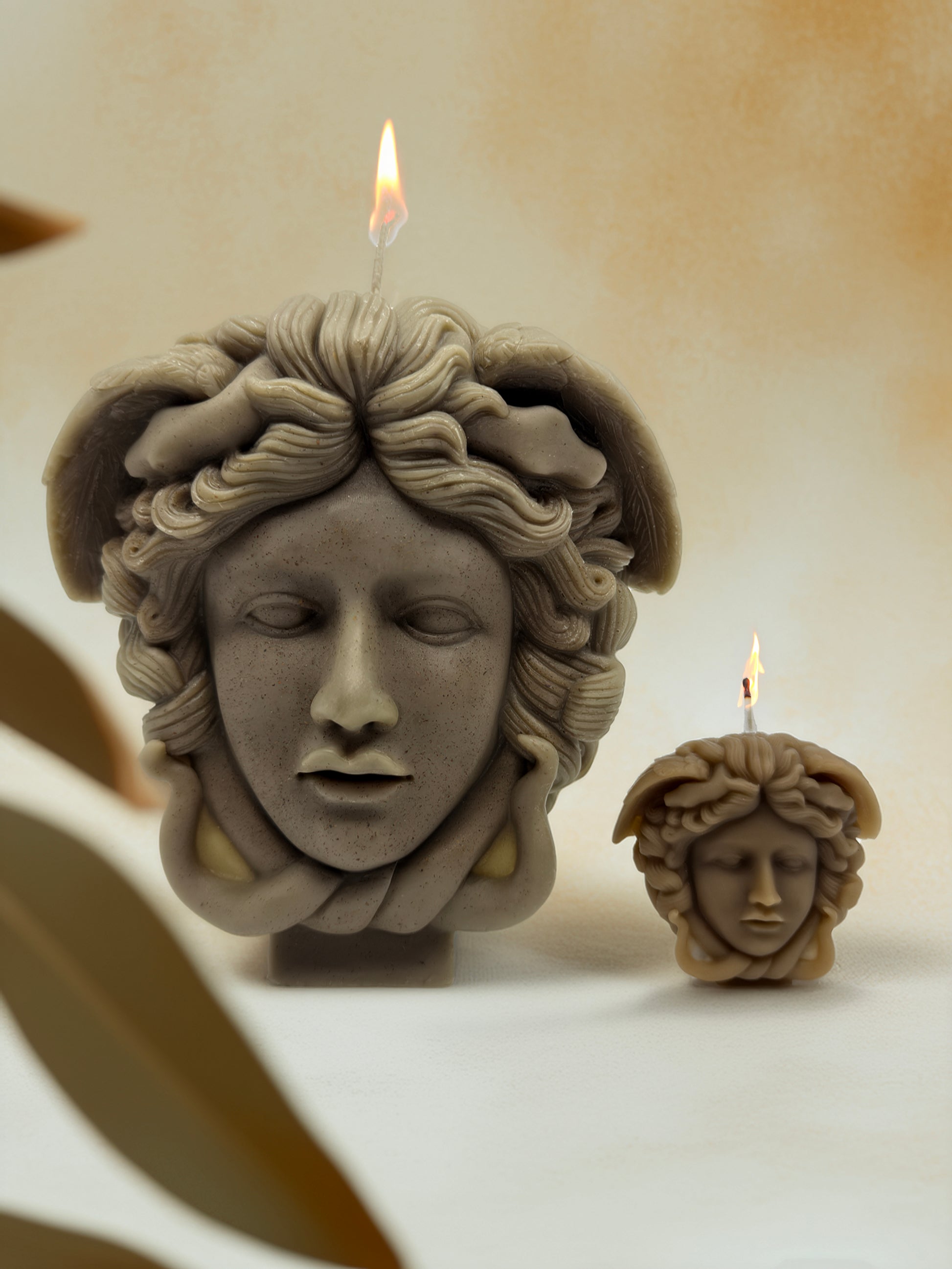 Two stone-like face candles with wreaths on a neutral background