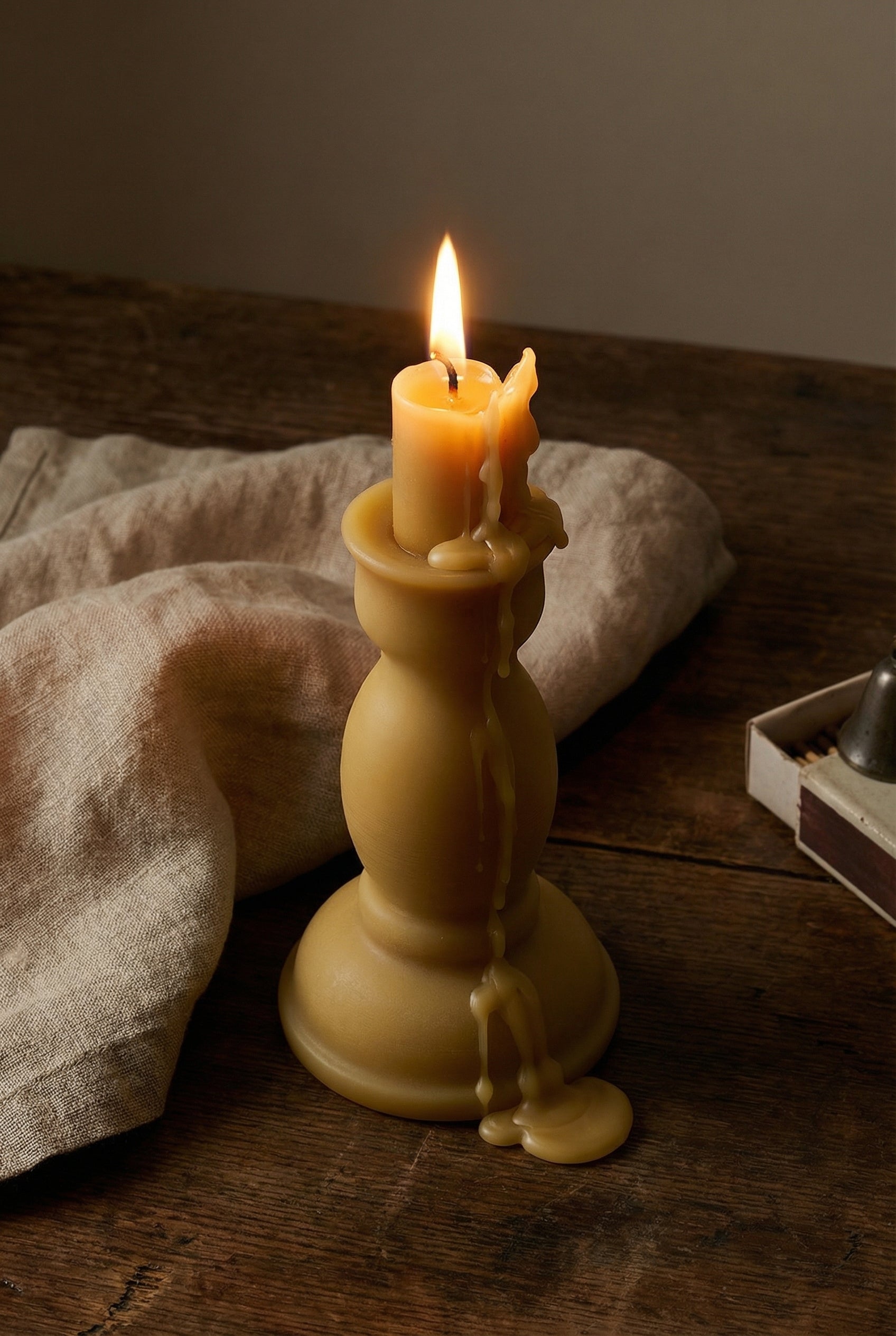 Pillar beeswax candle melting, linen, matches, wooden table