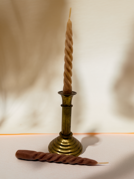 Brass candlestick holder with a twisted candle on a plain background